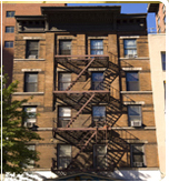 A picture of an old or vintage apartment building. Built-in red-orange brick. Each division or apartment rooms has a crystal sliding windows. There is a rusty-colored ladder or a stairway outside the apartment building from the top up to the bottom part of the building.